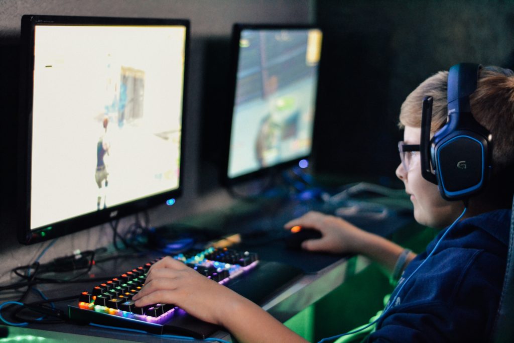 Kahdella näytöllä tietokonetta pelaava poika.  