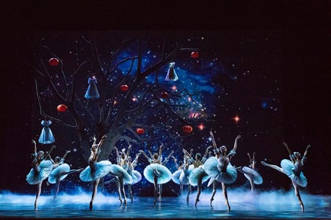 Balettitanssijoita lavalla, taustalla puu jossa roikkuu mekkoja ja kurpitsalyhtyjä.
