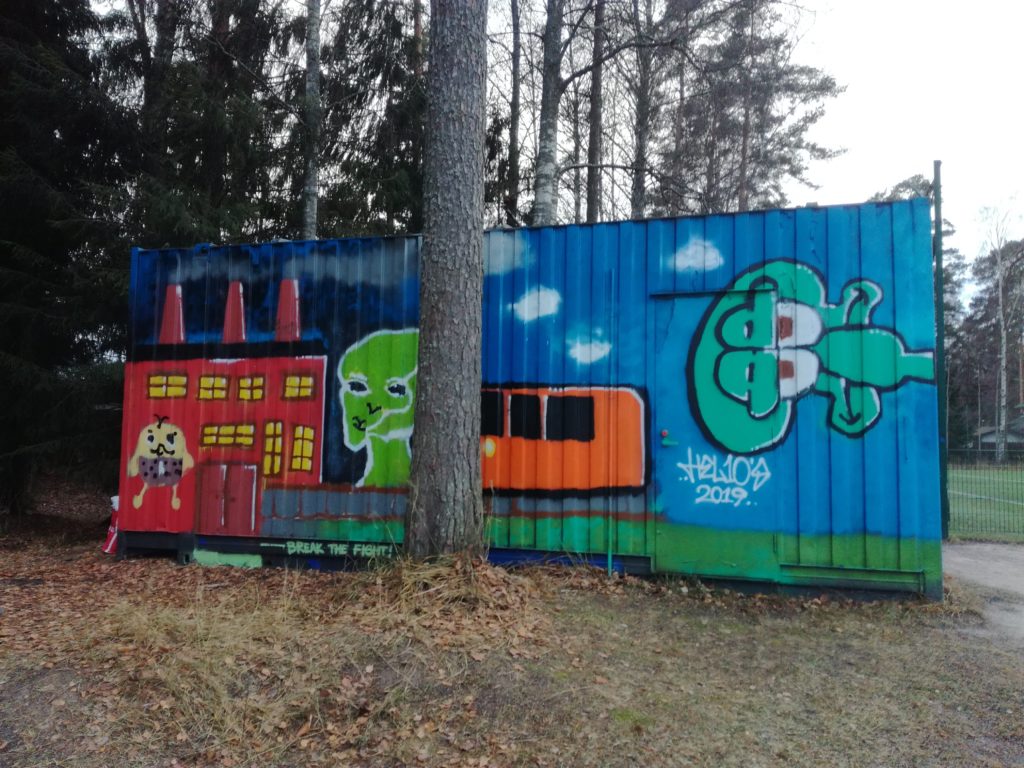 Graffititeos kontin seinässä metsäisessä ympäristössä.