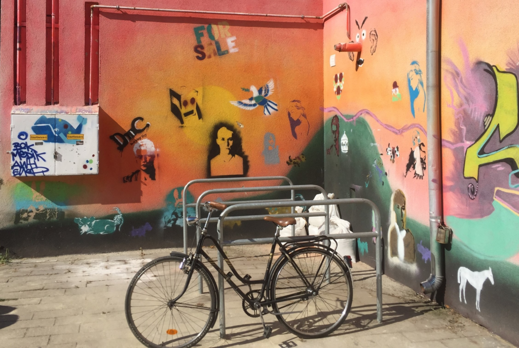 Vanha polkupyörä sisäpihalla, jonka seinät ovat lohenpunaiset ja joihin on maalattu graffiteja.