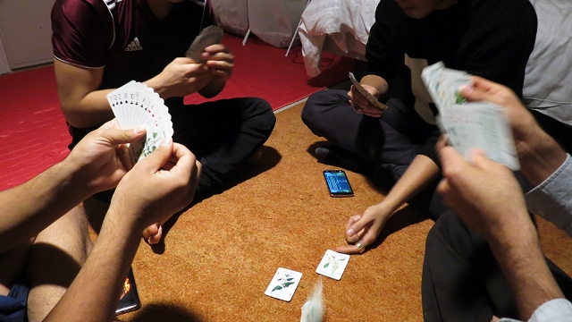 ihmisiä istumassa lattialla ja pelaamassa korttia.