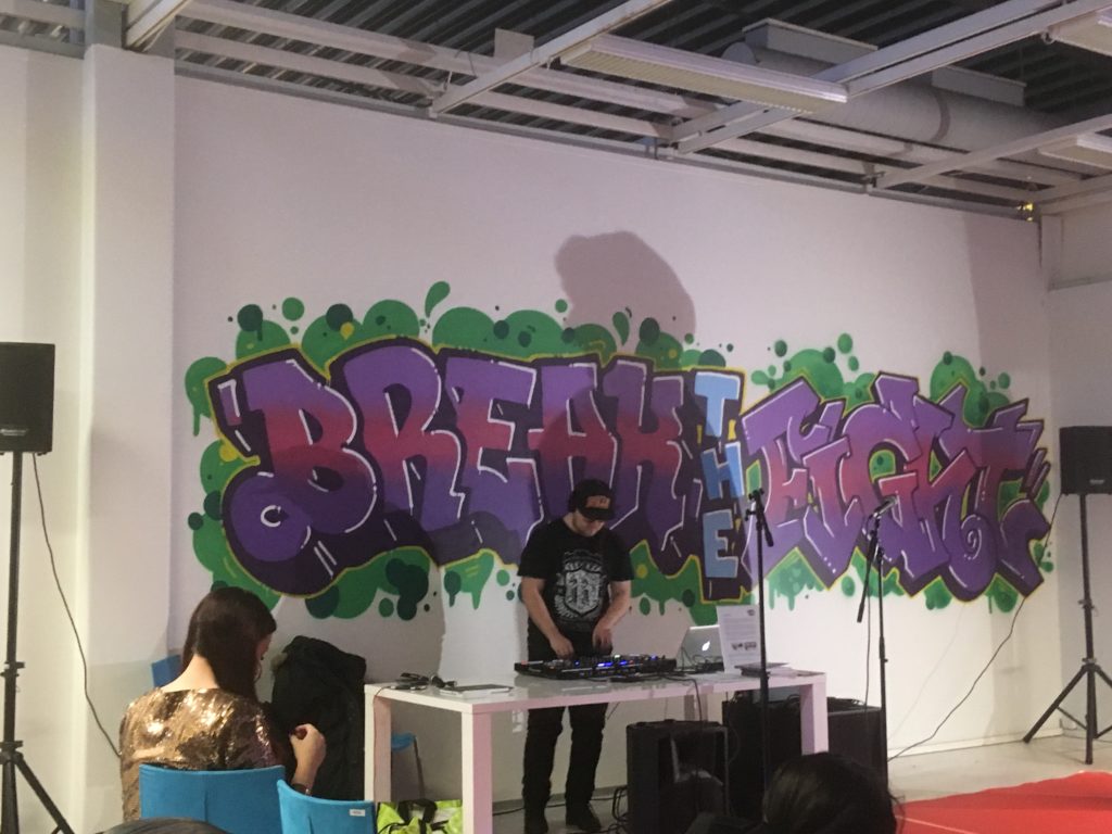 Kuva harrastetilan sisältä, huoneessa henkilö dj-pöydän takana ja seinällä teksti "break the fight". 