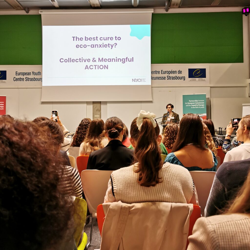 Photo from the plenary session, where a slide behind the speaker reads "the best cure to eco-anxiety."